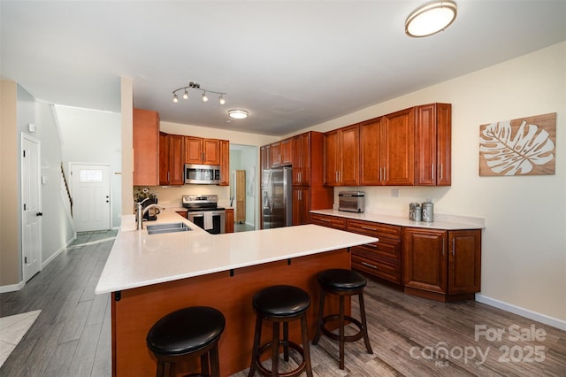 kitchen featuring appliances with stainless steel finishes, dark wood-type flooring, a breakfast bar, sink, and kitchen peninsula