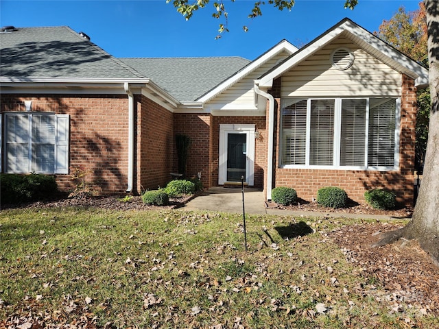 view of front of home featuring brick siding, a front lawn, and a shingled roof