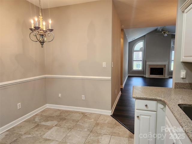 kitchen featuring baseboards, lofted ceiling, a fireplace, white cabinetry, and ceiling fan with notable chandelier