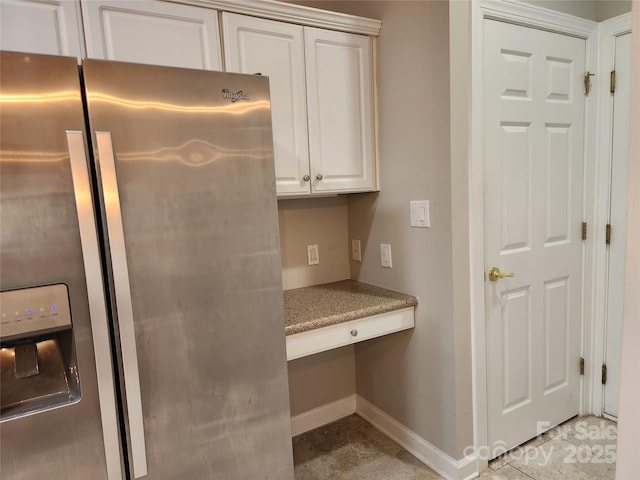 interior space featuring baseboards, light stone counters, built in desk, white cabinets, and stainless steel fridge