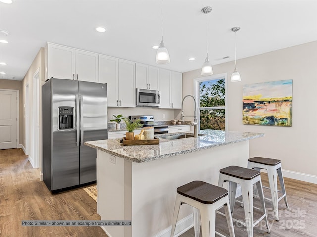 kitchen with light stone countertops, appliances with stainless steel finishes, white cabinets, sink, and a center island with sink