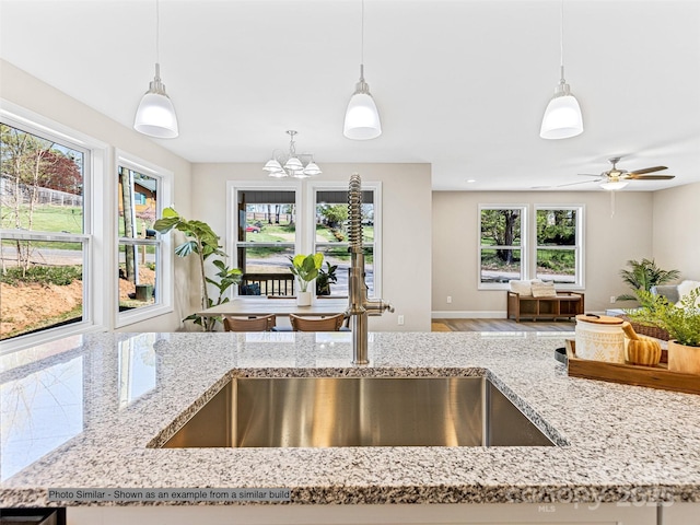 kitchen featuring ceiling fan with notable chandelier, hanging light fixtures, and light stone counters