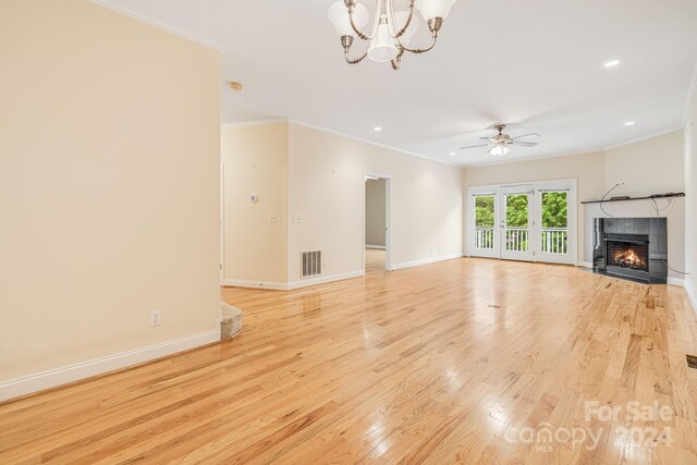 unfurnished living room with ceiling fan with notable chandelier, ornamental molding, a tiled fireplace, and light hardwood / wood-style flooring