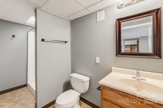 bathroom featuring vanity, toilet, a drop ceiling, walk in shower, and tile patterned flooring