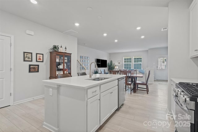 kitchen with appliances with stainless steel finishes, white cabinetry, an island with sink, sink, and light hardwood / wood-style floors