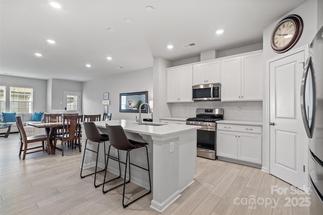 kitchen with sink, white cabinetry, appliances with stainless steel finishes, an island with sink, and decorative backsplash