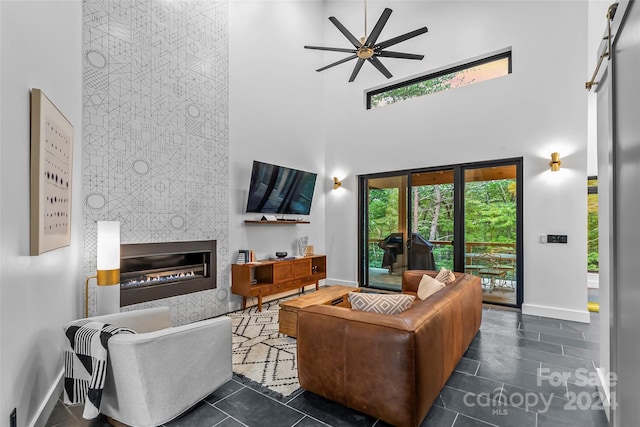 tiled living area featuring baseboards, a high ceiling, ceiling fan, and a tile fireplace