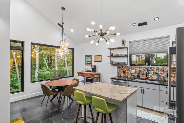 kitchen with pendant lighting, sink, dishwasher, dark stone countertops, and a notable chandelier