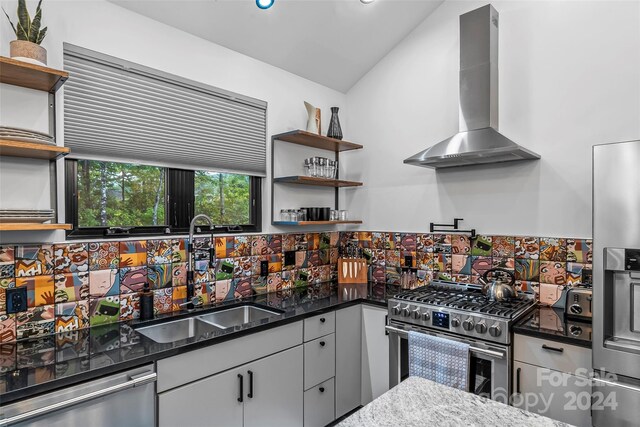 kitchen with lofted ceiling, sink, wall chimney range hood, stainless steel appliances, and dark stone countertops