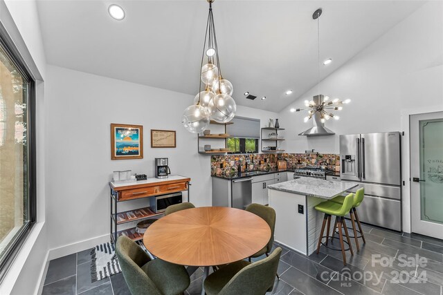 dining space featuring sink, high vaulted ceiling, dark tile patterned flooring, and a notable chandelier