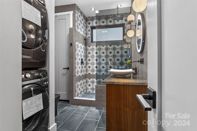 bathroom featuring vanity, tiled shower, stacked washer and clothes dryer, tile patterned floors, and toilet