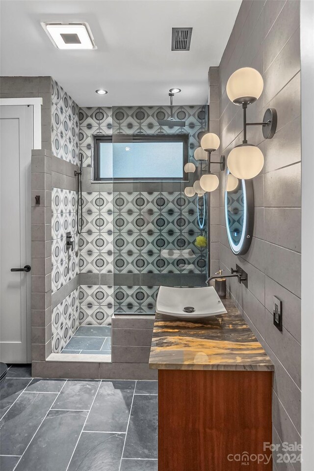 bathroom with tile walls, tile patterned floors, a shower, and vanity