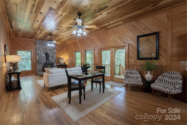 dining area with hardwood / wood-style flooring, a wood stove, vaulted ceiling, wood walls, and ceiling fan