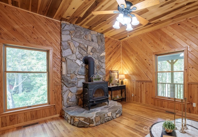 living room with ceiling fan, lofted ceiling, a wood stove, wooden walls, and hardwood / wood-style flooring