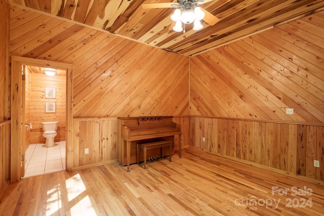 bonus room featuring light wood-type flooring, wood walls, ceiling fan, and vaulted ceiling