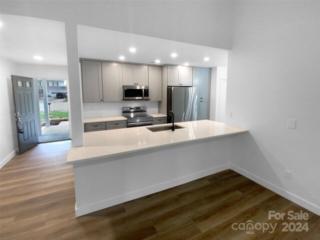 kitchen with kitchen peninsula, appliances with stainless steel finishes, dark hardwood / wood-style floors, and sink