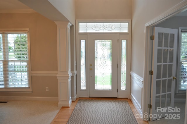 foyer entrance featuring ornate columns, light hardwood / wood-style flooring, and ornamental molding