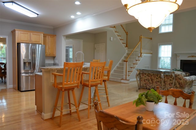 kitchen featuring crown molding, stainless steel refrigerator with ice dispenser, light stone countertops, light brown cabinetry, and light hardwood / wood-style floors