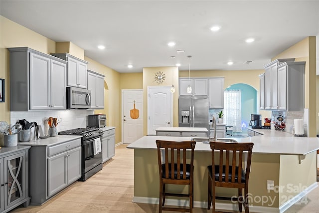 kitchen with decorative backsplash, appliances with stainless steel finishes, a kitchen breakfast bar, light hardwood / wood-style flooring, and gray cabinets