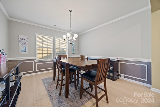 dining space with crown molding, light hardwood / wood-style flooring, and an inviting chandelier