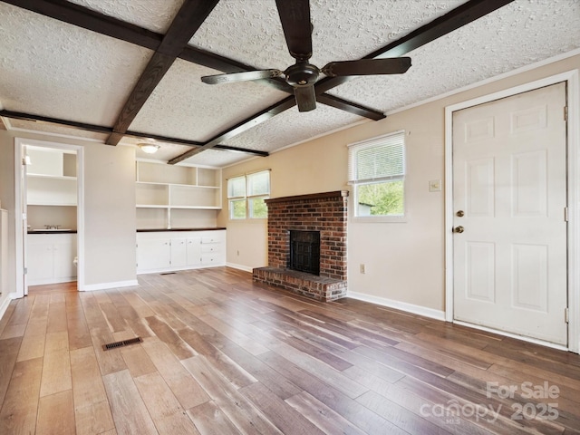 unfurnished living room featuring beam ceiling, ceiling fan, coffered ceiling, a brick fireplace, and hardwood / wood-style floors