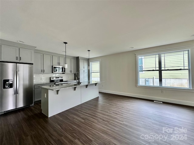 kitchen with a healthy amount of sunlight, a kitchen island with sink, light stone countertops, gray cabinetry, and stainless steel appliances