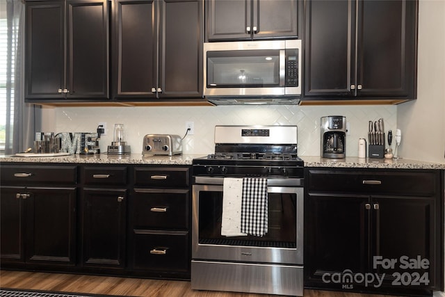 kitchen with stainless steel appliances, light stone counters, and light wood-type flooring