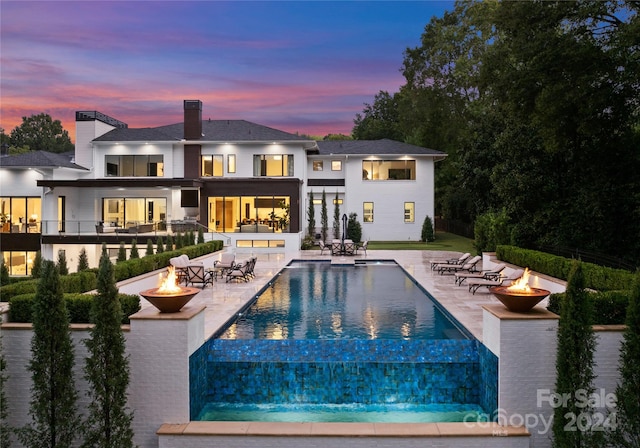 back house at dusk with a balcony, a patio, and an outdoor fire pit