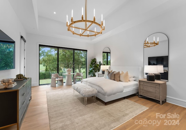 bedroom featuring light wood-type flooring, a raised ceiling, access to exterior, and a notable chandelier