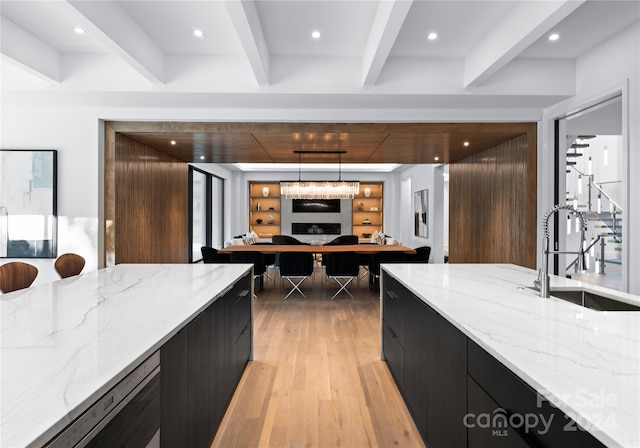 kitchen featuring light stone counters, pendant lighting, beam ceiling, sink, and light wood-type flooring