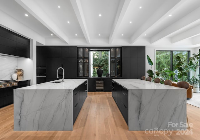 kitchen with beam ceiling, plenty of natural light, a large island with sink, and sink