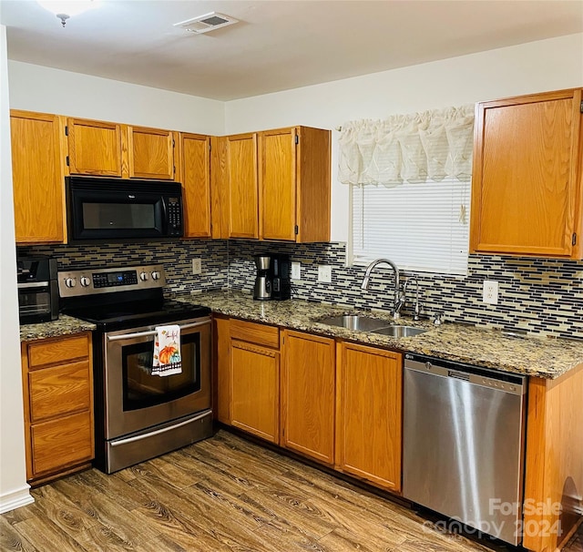 kitchen featuring sink, tasteful backsplash, wood-type flooring, stone counters, and appliances with stainless steel finishes