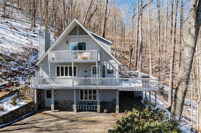 snow covered rear of property with a balcony, a chimney, and a deck