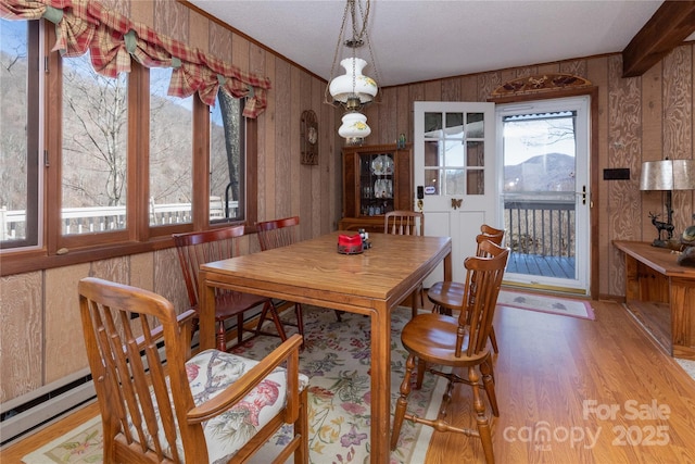 dining area with a baseboard radiator, wooden walls, crown molding, and wood finished floors