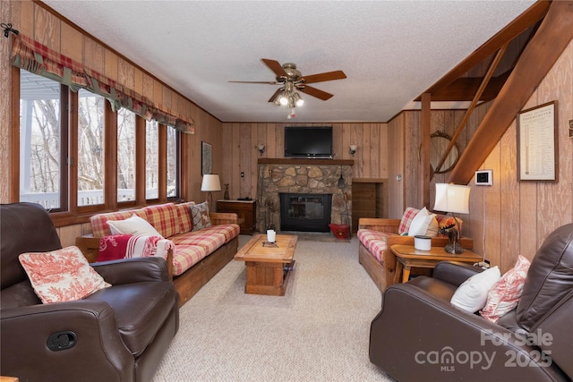 carpeted living area featuring wood walls, a textured ceiling, a ceiling fan, and a stone fireplace