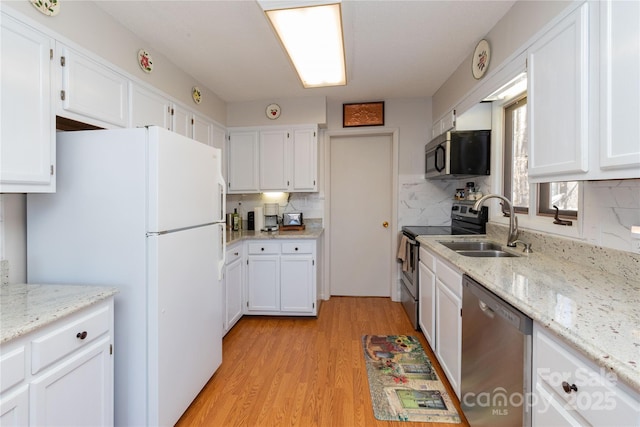 kitchen with appliances with stainless steel finishes, light wood-style floors, white cabinetry, a sink, and light stone countertops