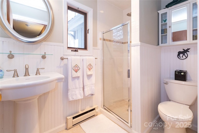 bathroom featuring toilet, a baseboard heating unit, a stall shower, wainscoting, and a sink