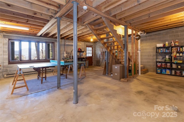 below grade area with concrete block wall, a baseboard radiator, and stairs