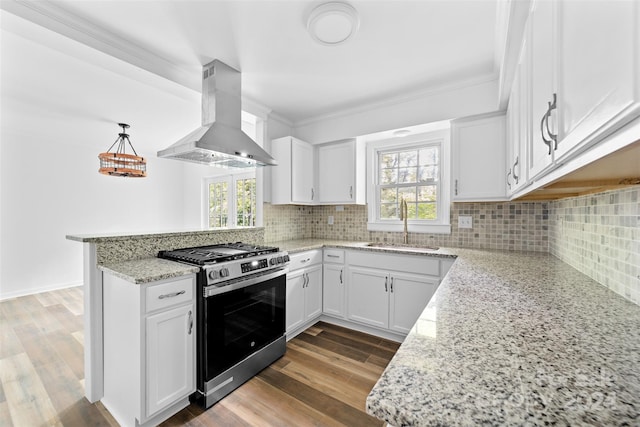 kitchen with white cabinets, kitchen peninsula, decorative light fixtures, stainless steel gas range, and wall chimney range hood