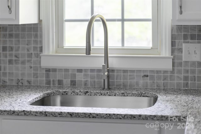 interior details with light stone counters, sink, and decorative backsplash