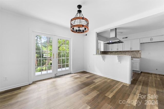 kitchen featuring kitchen peninsula, island range hood, decorative light fixtures, white cabinetry, and dark hardwood / wood-style floors