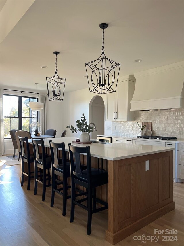 kitchen featuring premium range hood, a large island, a chandelier, white cabinetry, and light wood-type flooring