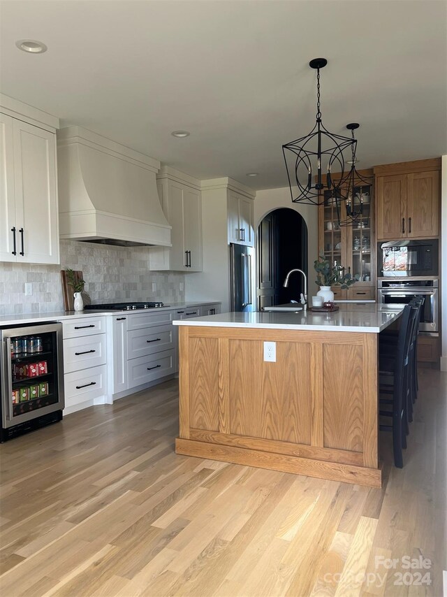 kitchen with premium range hood, a large island, beverage cooler, white cabinetry, and appliances with stainless steel finishes