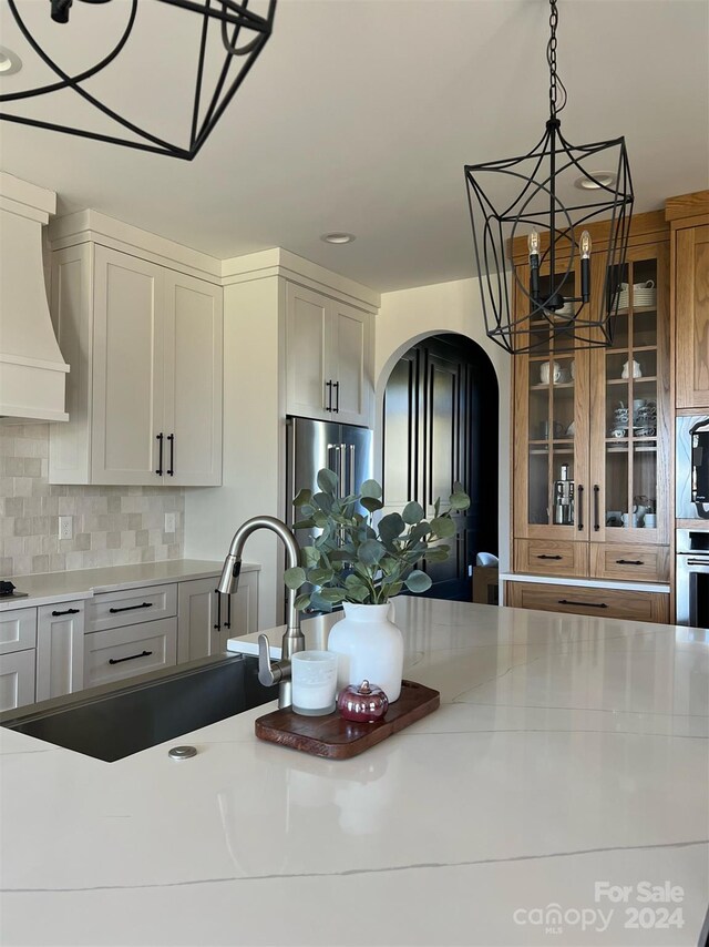 kitchen with a chandelier, sink, custom range hood, stainless steel appliances, and backsplash