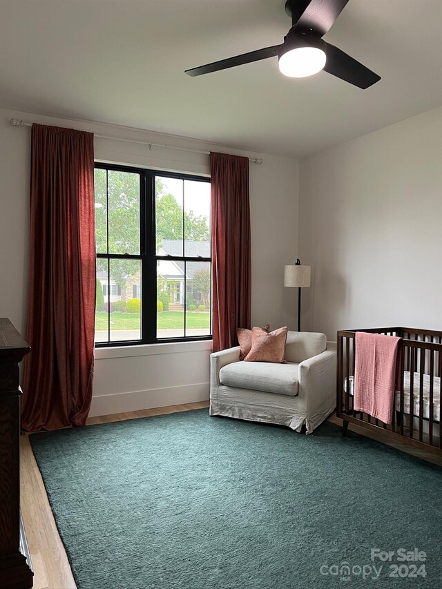 bedroom with wood-type flooring, ceiling fan, and a nursery area