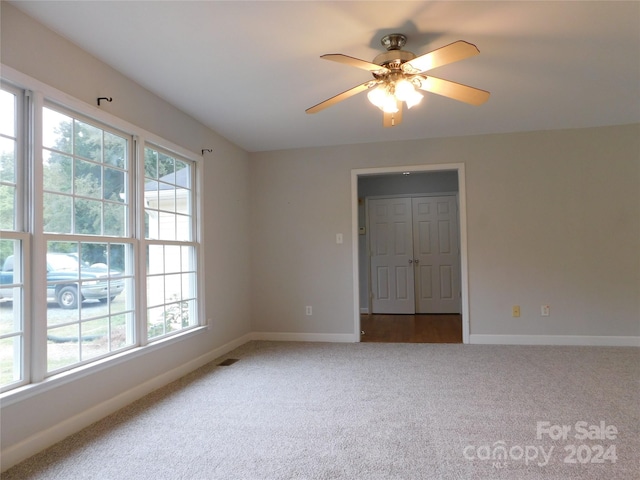 empty room featuring baseboards, visible vents, dark carpet, and ceiling fan