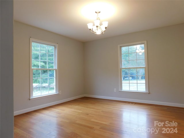 spare room featuring a chandelier, a wealth of natural light, and light wood finished floors