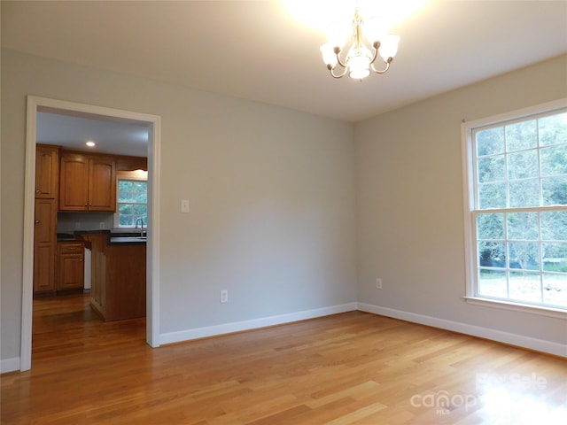 empty room with a chandelier, sink, light hardwood / wood-style flooring, and a wealth of natural light