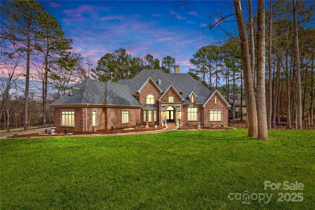 view of front of home featuring a yard, brick siding, and roof with shingles