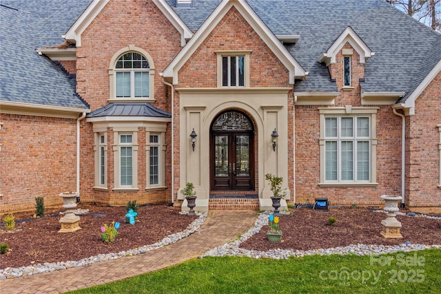 doorway to property featuring brick siding, french doors, and roof with shingles